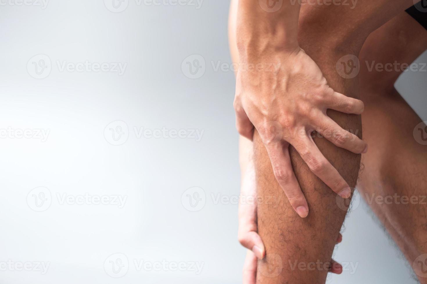 maschio adulto con il suo dolore muscolare su sfondo grigio. uomo anziano che ha dolore alle gambe a causa della trazione muscolare del polpaccio. lesioni sportive e concetto medico foto