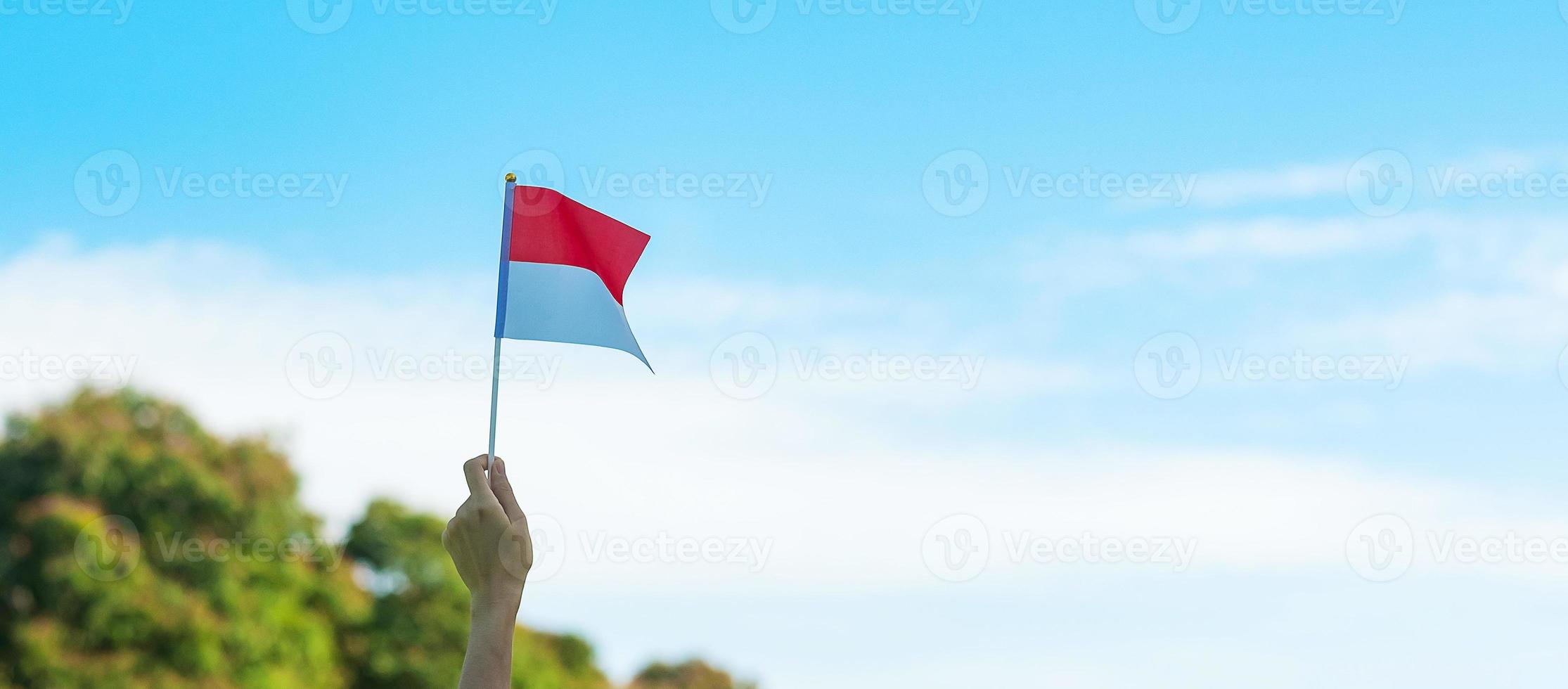 mano che tiene la bandiera dell'indonesia su sfondo blu cielo. giorno dell'indipendenza dell'indonesia, festa nazionale e concetti di celebrazione felice foto