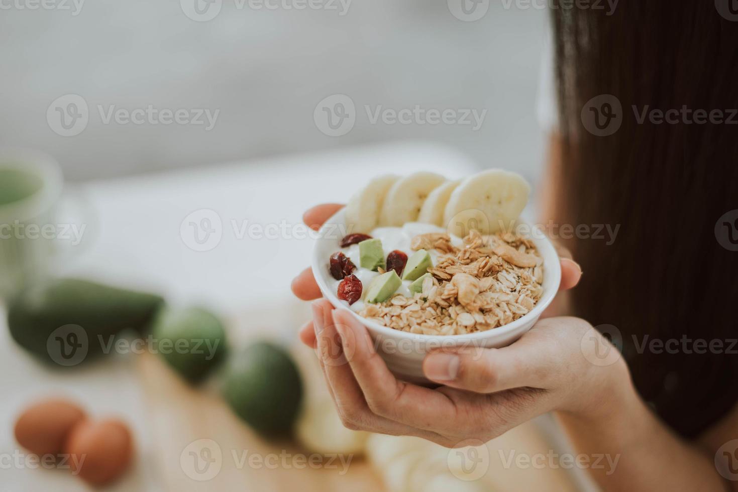 primo piano delle mani della donna che tengono i fiocchi di muesli nella ciotola. giovane donna che cucina cibo sano a casa. concetto di salute e benessere. foto