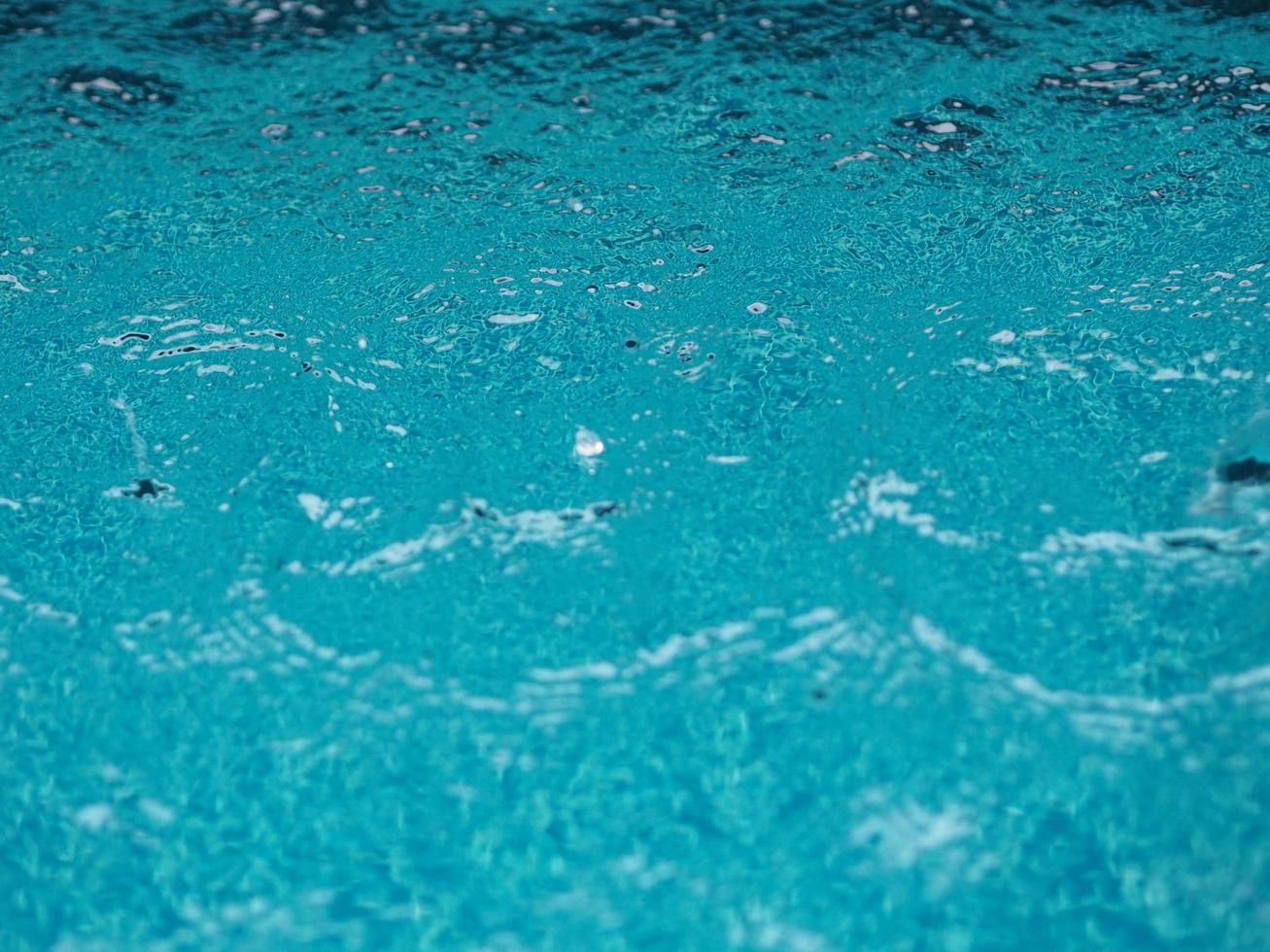 gocce di pioggia che cadono acqua blu sullo sfondo della piscina increspature sulla struttura della superficie, scintillante bokeh astratto foto