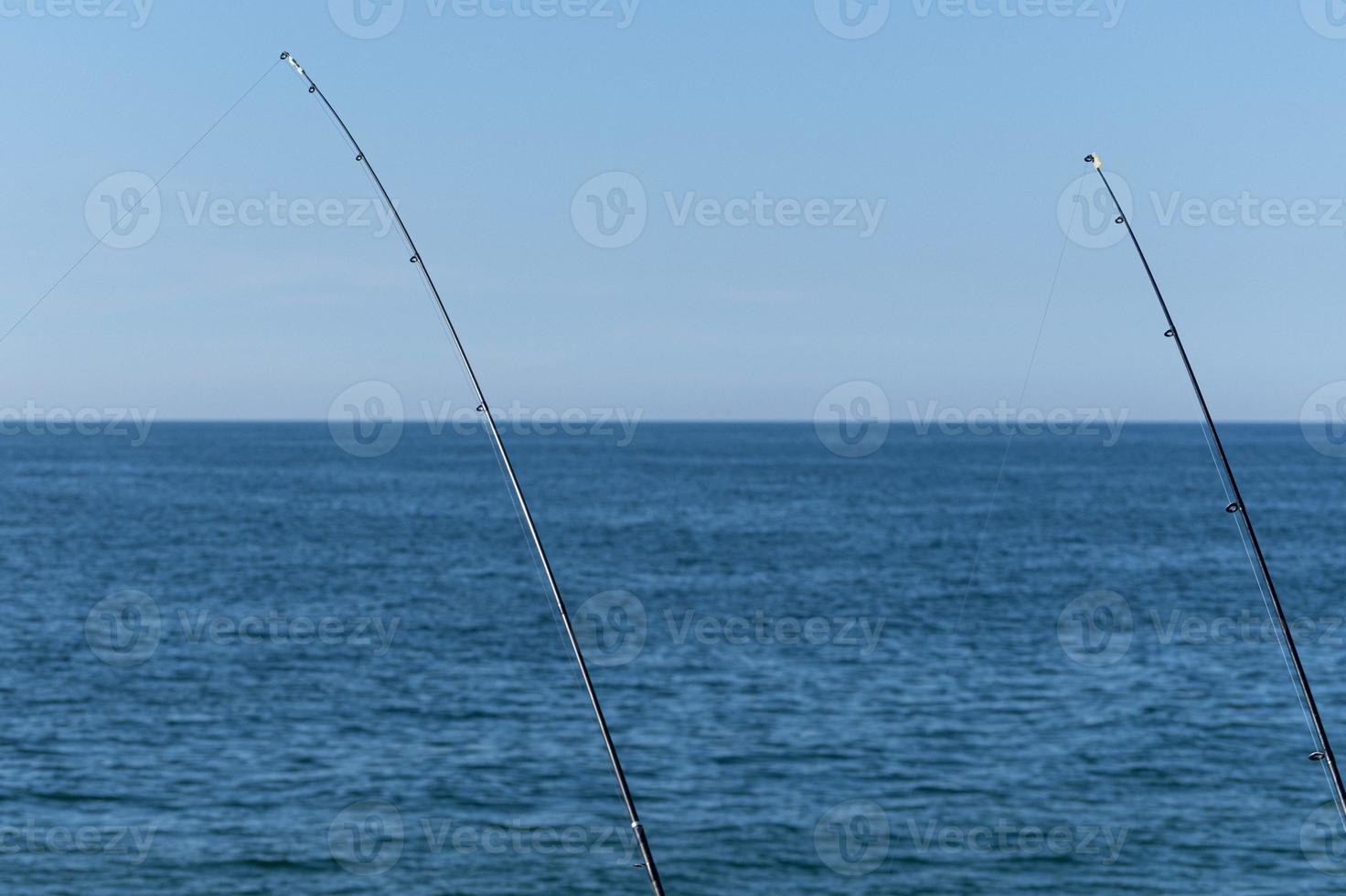 due canne da pesca sullo sfondo blu dell'oceano o del mare, spazio di copia. aspettando il bottino più grande. sport di rilassamento meditativo. foto