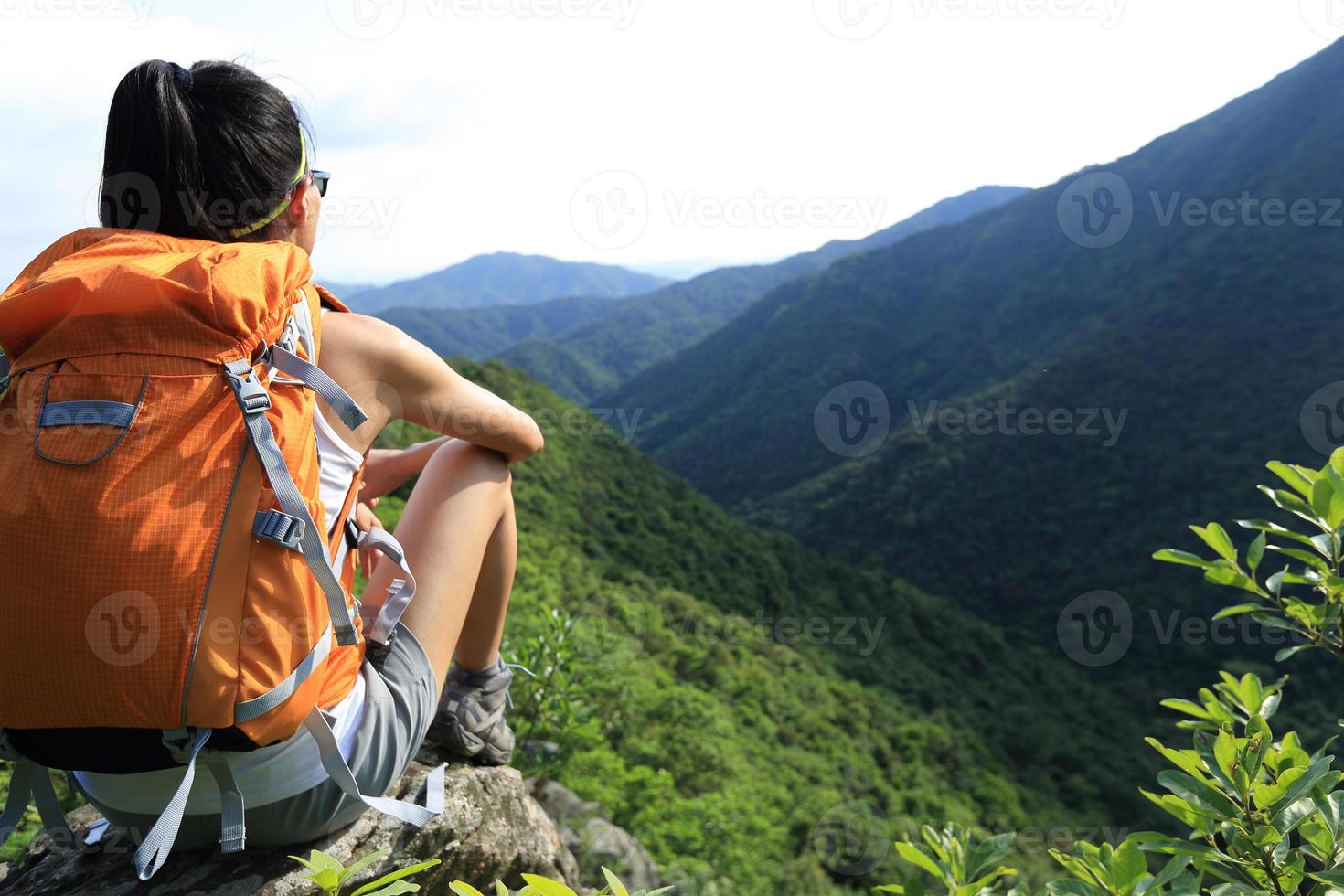 il viaggiatore con zaino e sacco a pelo della donna gode della vista alla scogliera del picco di montagna foto