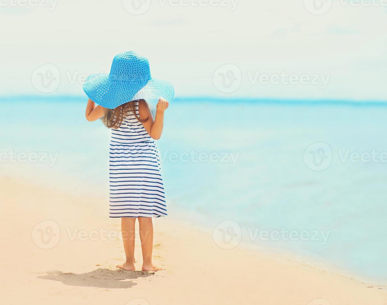 bambina graziosa in vestito e cappello di paglia che gode del mare foto