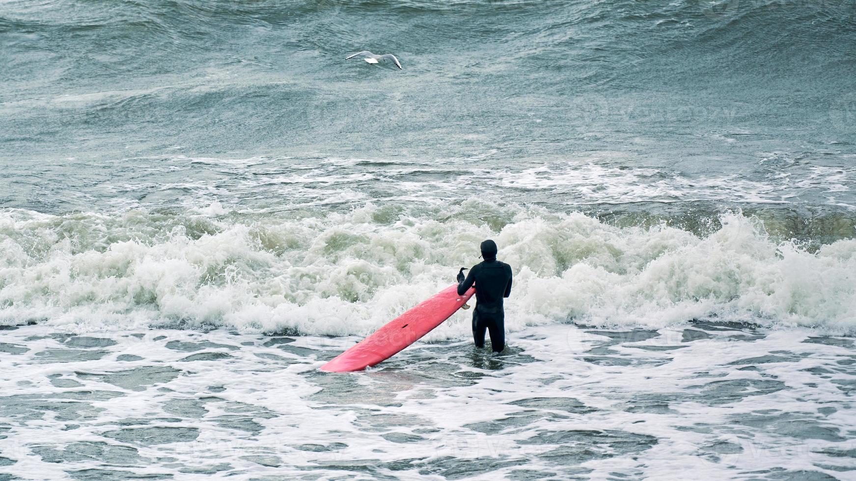 surfista maschio in costume da bagno nelle onde del mare con tavola da surf rossa foto