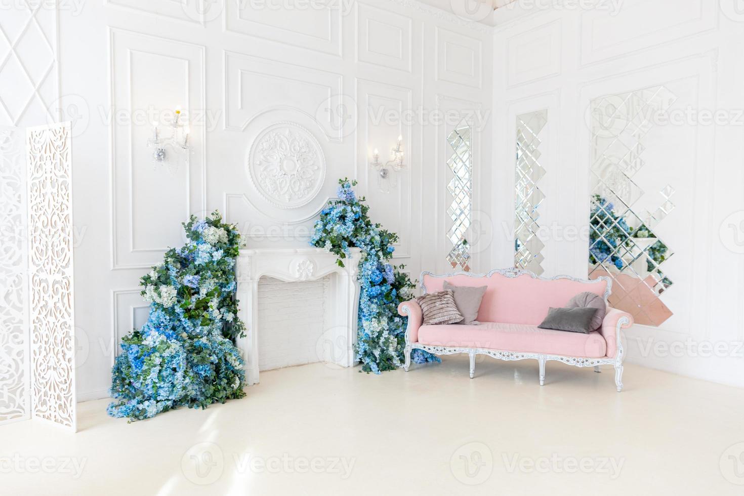 bellissimo soggiorno interno pulito classico di lusso in colore bianco con composizione floreale di fiori divano divano rosa. luminoso soggiorno interno moderno ed elegante con mobili in stile classico minimalista. foto