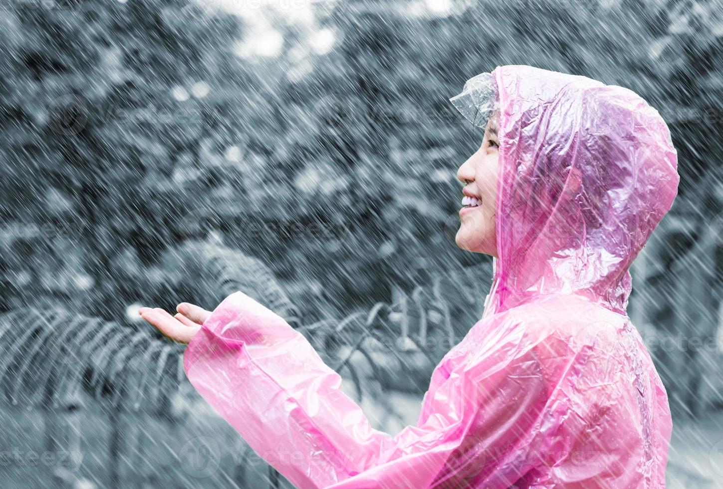 donna asiatica in impermeabile rosa godendo la pioggia in giardino foto
