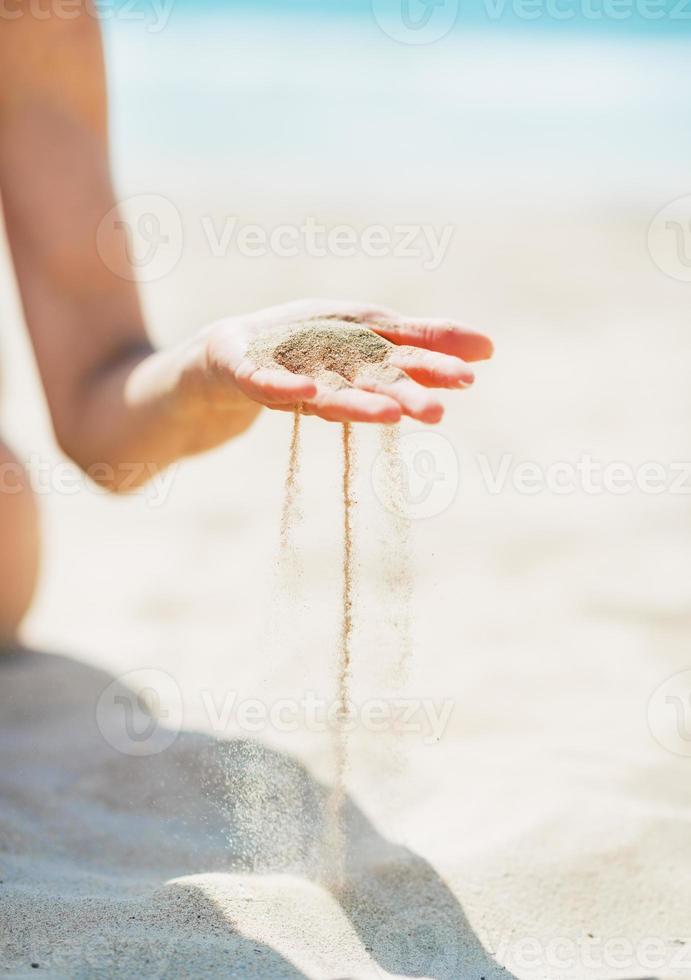 giovane donna seduta sulla spiaggia e giocare con la sabbia. avvicinamento foto