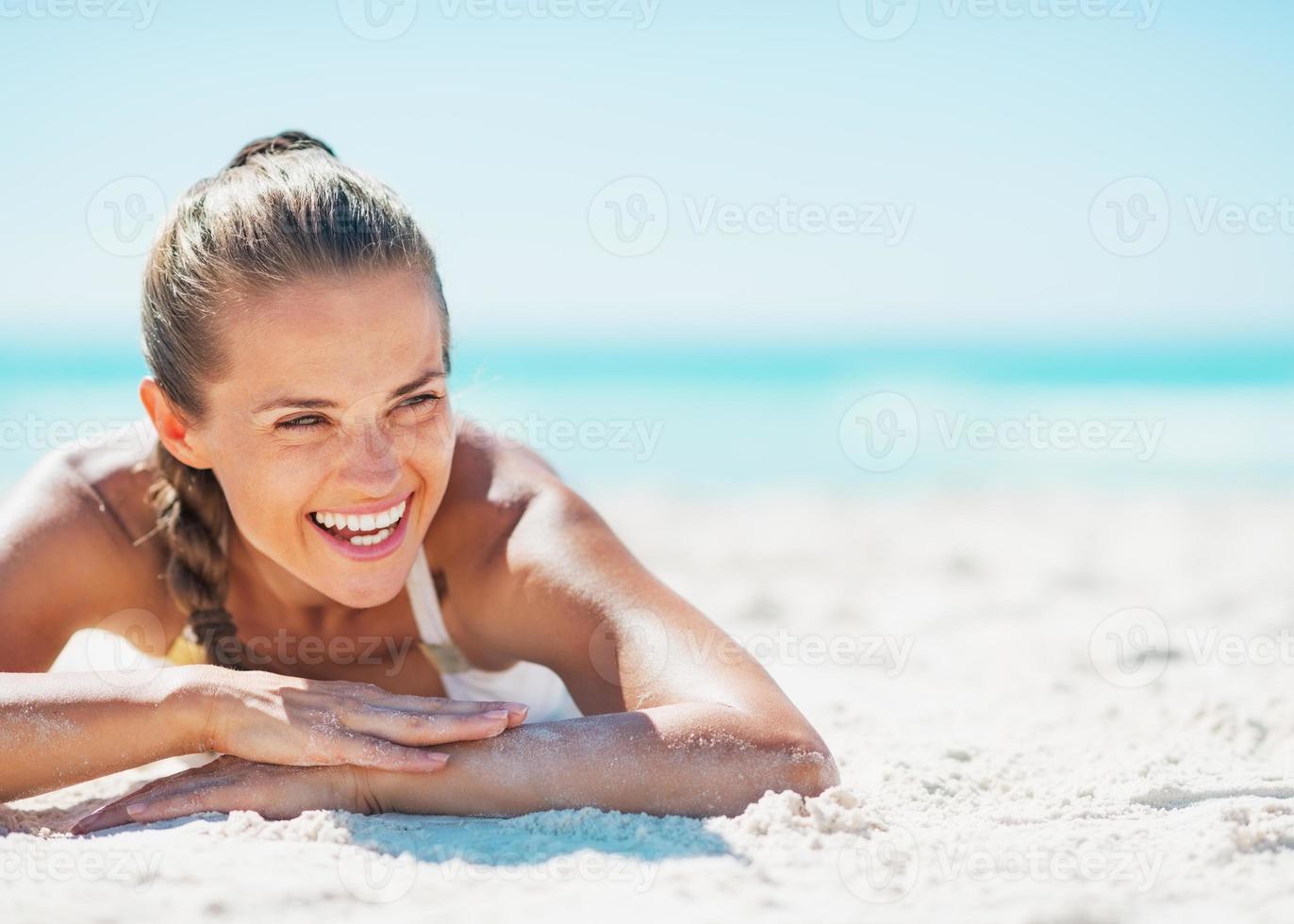 giovane donna sorridente in costume da bagno godendo posa sulla spiaggia foto