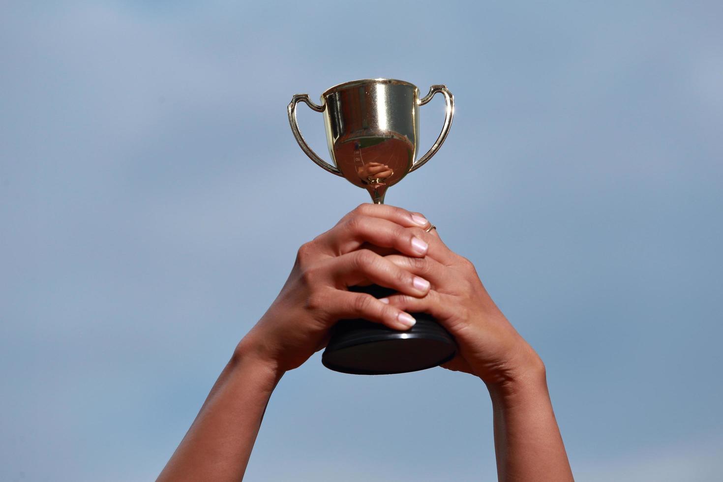 un successo vincitore che celebra con il premio del trofeo e il concetto di campione, tenendo a mano il trofeo del campionato contro il cielo blu. foto