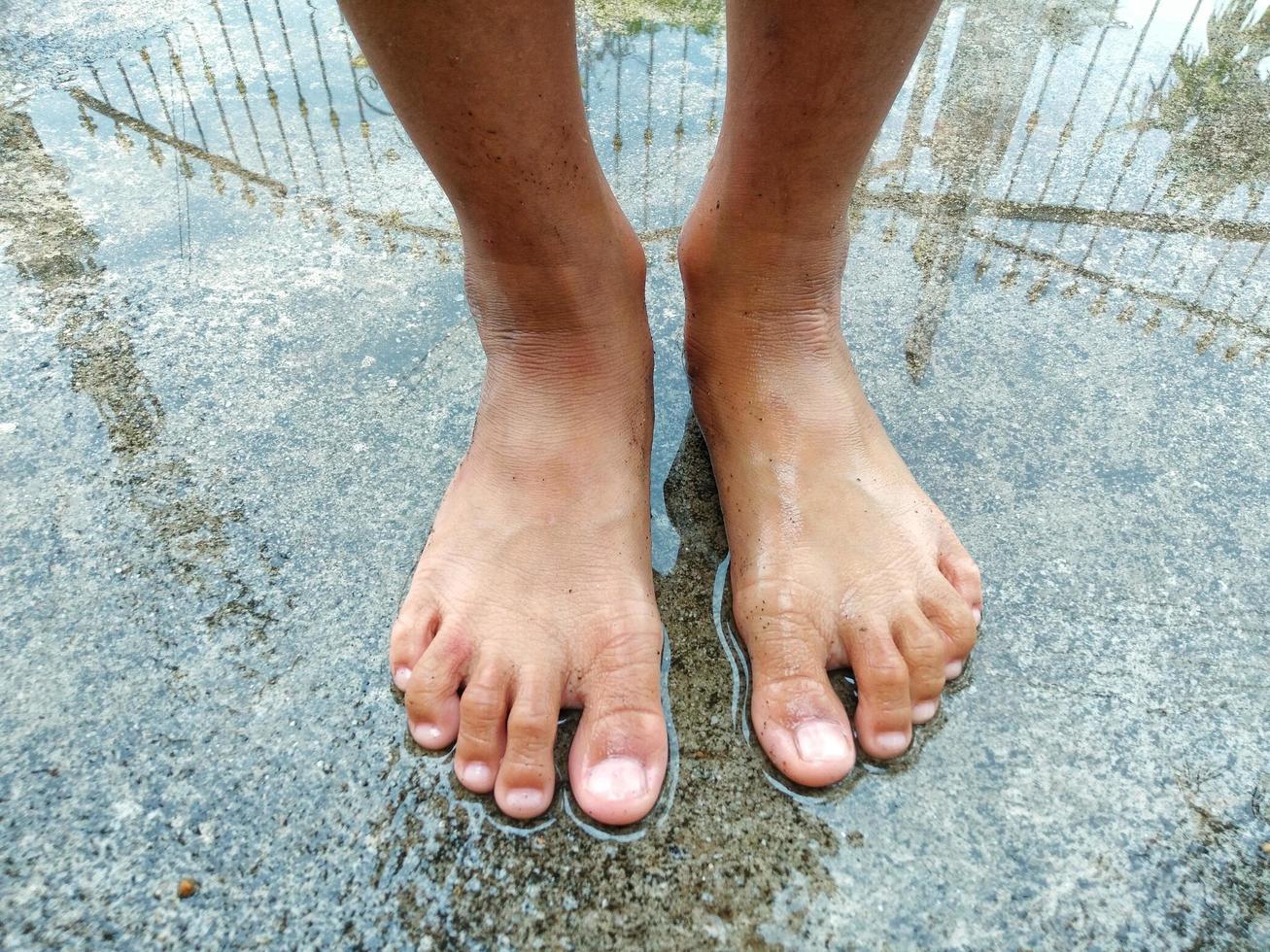 i piedi del bambino sono in una pozzanghera su un vecchio pavimento di cemento davanti alla casa. dopo una forte pioggia per divertirsi foto