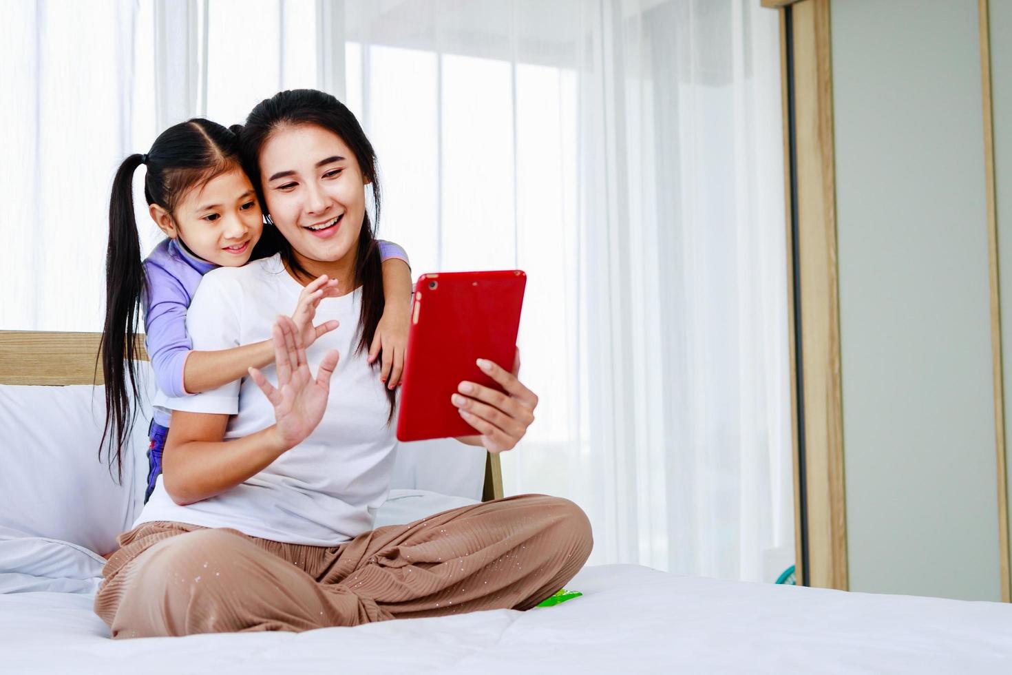 la madre felice con la bambina sta facendo selfie o videochiamate a padre o parenti a letto foto