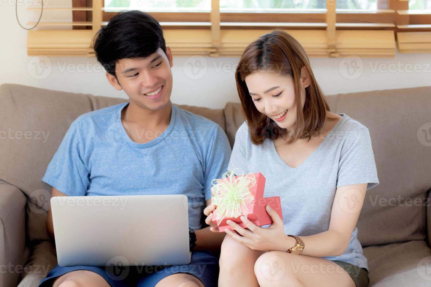 la giovane coppia asiatica festeggia il compleanno insieme, l'uomo asiatico regala una confezione regalo alla donna per una sorpresa in soggiorno, l'anniversario felice ed eccitato femminile, il concetto di San Valentino per le vacanze. foto