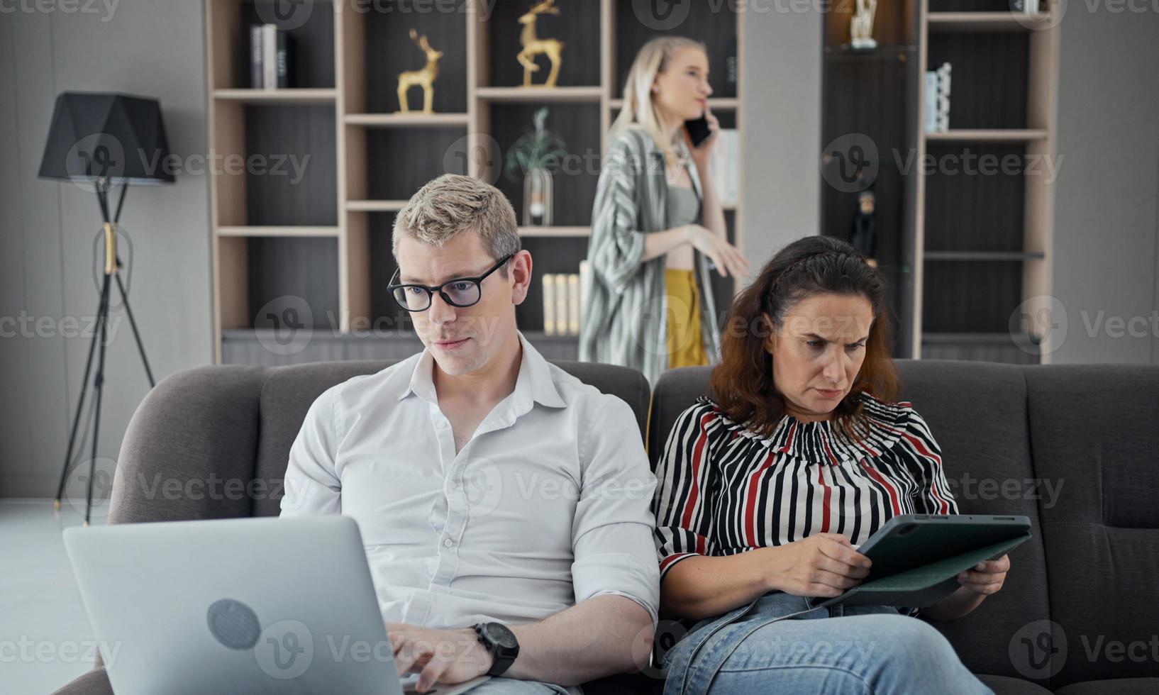 dipendenza da gadget. giovane caucasico di tre persone che tiene e utilizza diversi dispositivi elettronici mentre è seduto sul divano nel soggiorno di casa. genitori e la loro figlia con gadget moderni foto