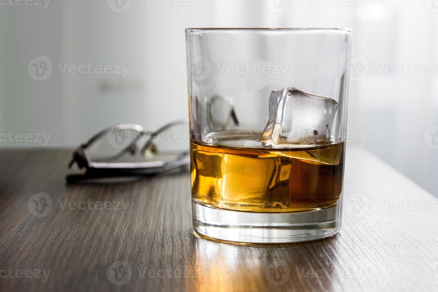 bicchiere di whisky, brandy, cognac con cubetti di ghiaccio su tavolo in legno scrivania con bicchieri. mockup di prodotto, regalo per uomo foto