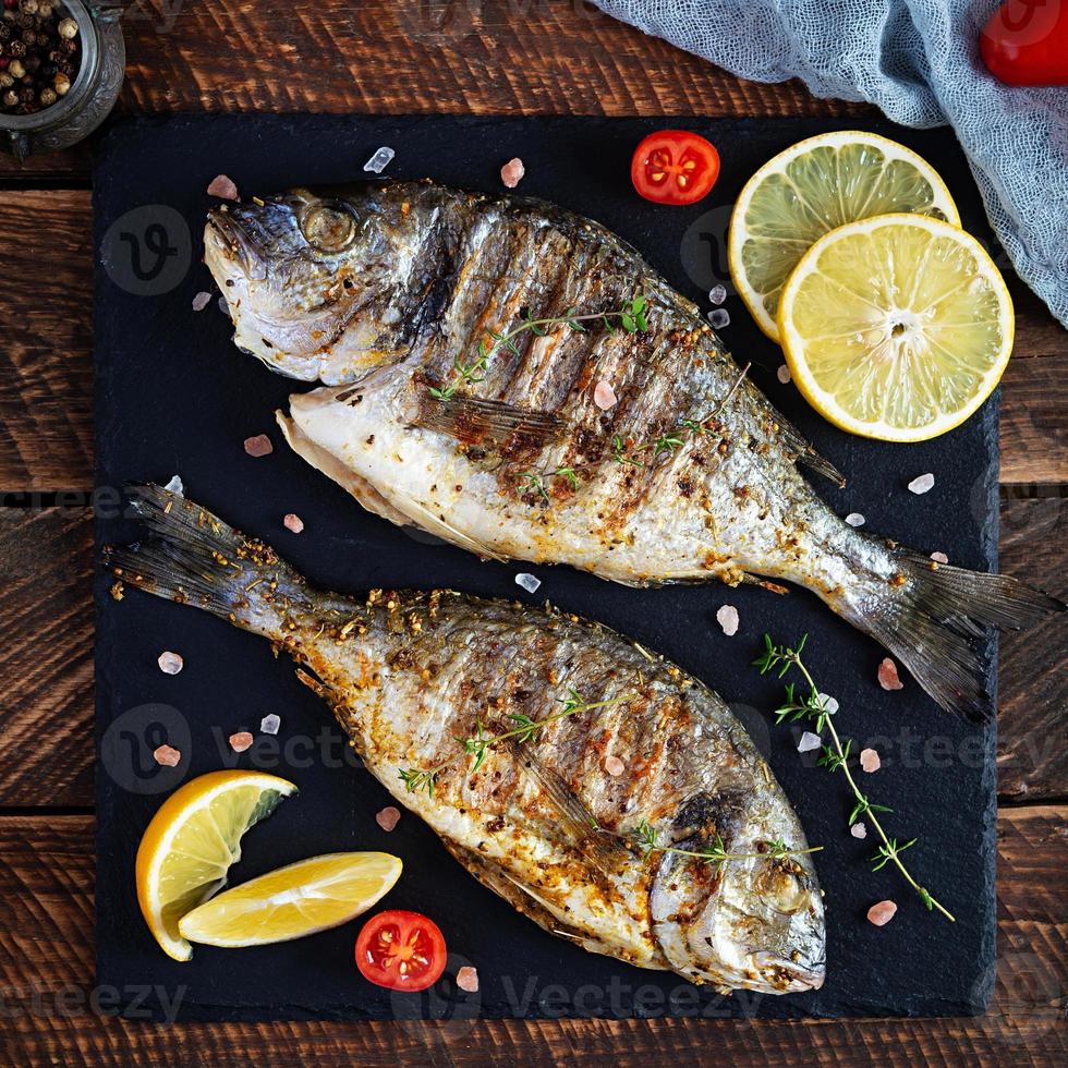 pesce dorado alla griglia su fondo di legno. pesce di mare arrosto con spezie ed erbe aromatiche foto