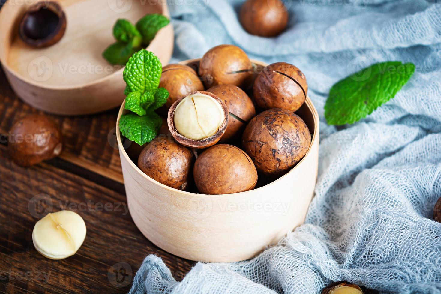 noci di macadamia in guscio con foglie di menta e miele su fondo di legno foto