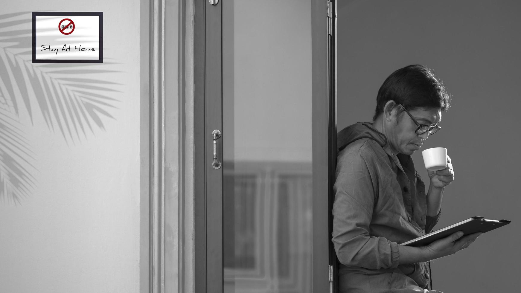 uomo asiatico che beve caffè caldo e guarda gli appunti nella cornice di una finestra di vetro a casa nel concetto di autoisolamento foto