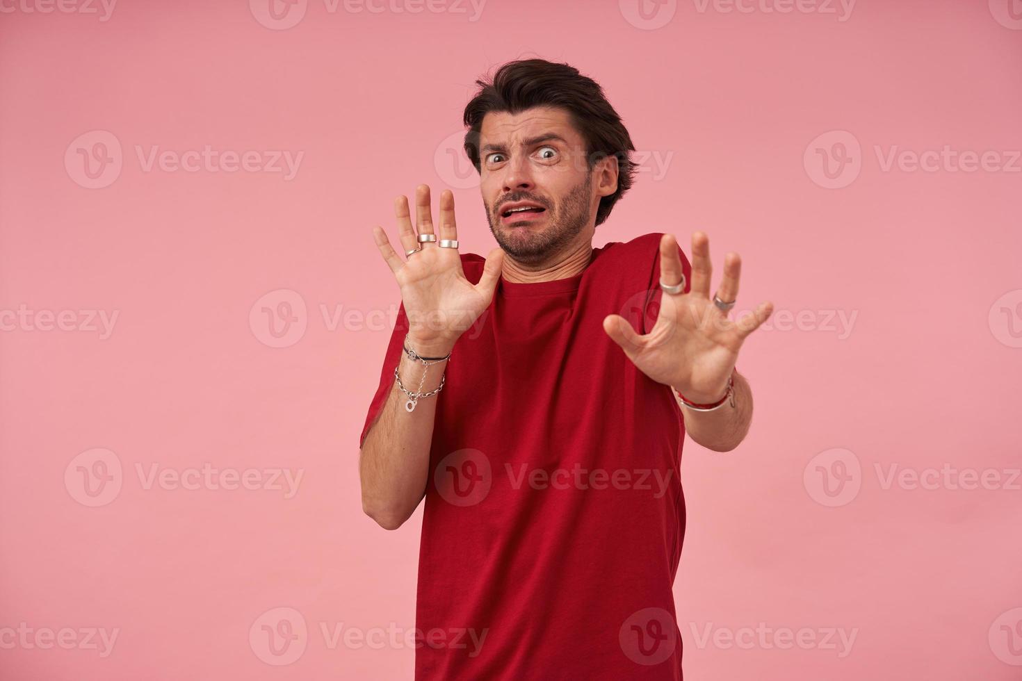 giovane spaventato spaventato con setole in maglietta rossa che fa un gesto spaventato con i palmi delle mani mentre cerca di difendersi su sfondo rosa foto