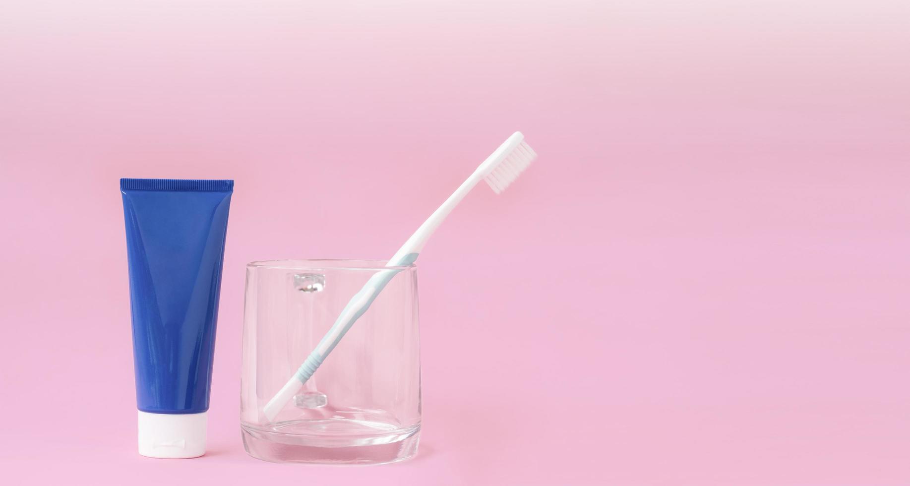 tubetto di dentifricio blu e spazzolino da denti in vetro trasparente con illuminazione sfumata su sfondo rosa pastello, primo piano con spazio per la copia foto