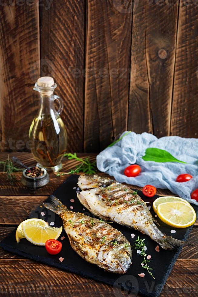 pesce dorado alla griglia su fondo di legno. pesce di mare arrosto con spezie ed erbe aromatiche foto