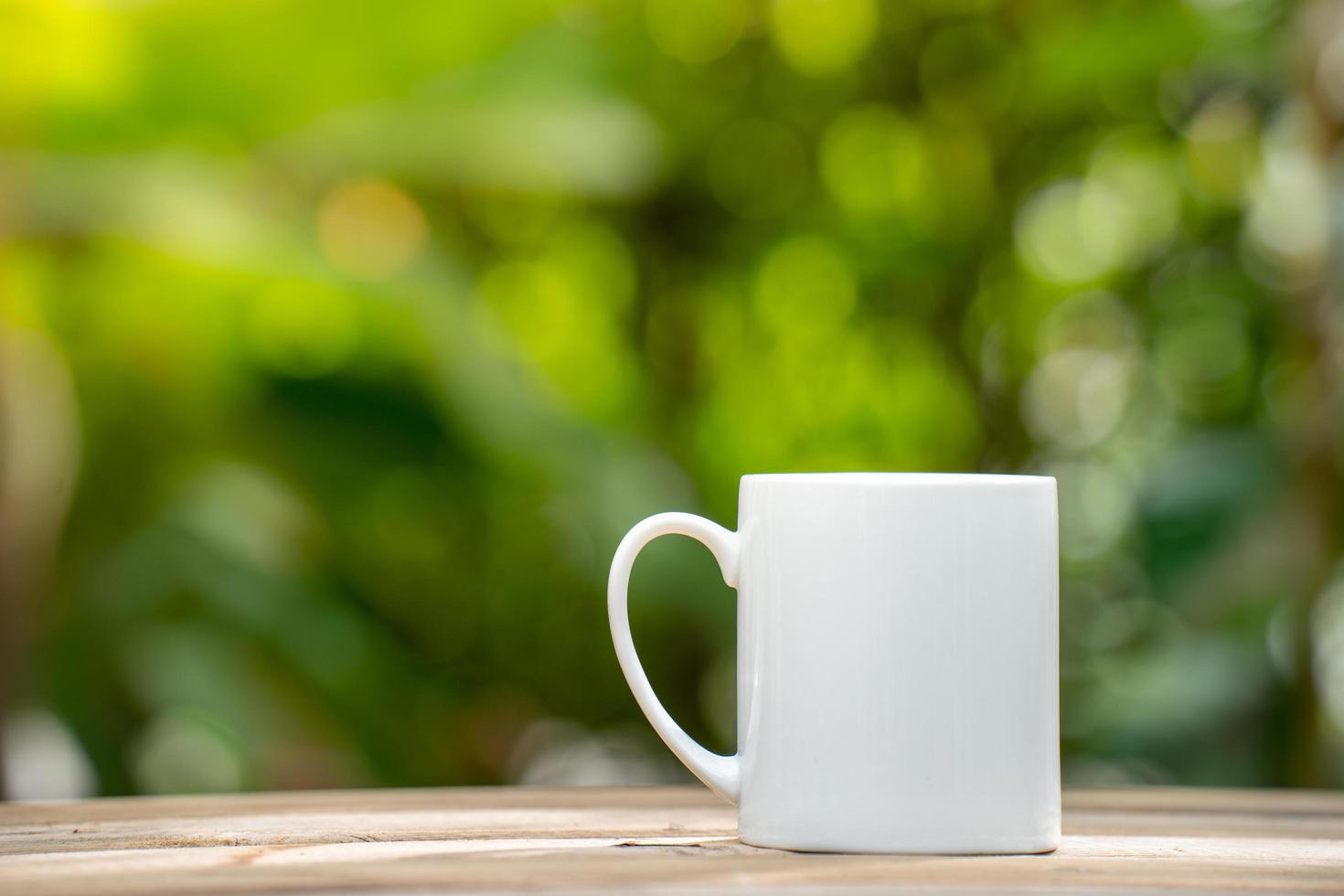 tazza da caffè in ceramica bianca sul pavimento di legno, sfondo bokeh albero verde. effetto messa a fuoco morbida. foto