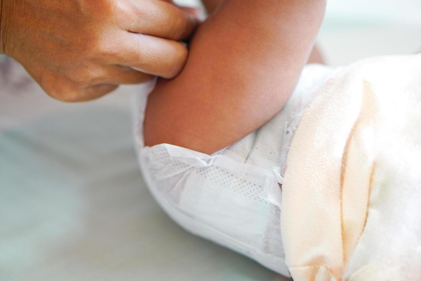 le mani della madre che cambiano il pannolino asiatico piccolo bambino o neonato in casa con amore, pulizia foto