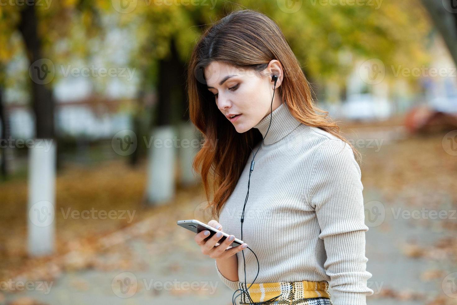 immagine di bella donna alla moda che tiene il telefono cellulare. giovane ragazza europea in piedi per strada e utilizzando il cellulare. donna che ascolta la musica con il telefono e si diverte. concetto di Internet mobile. foto