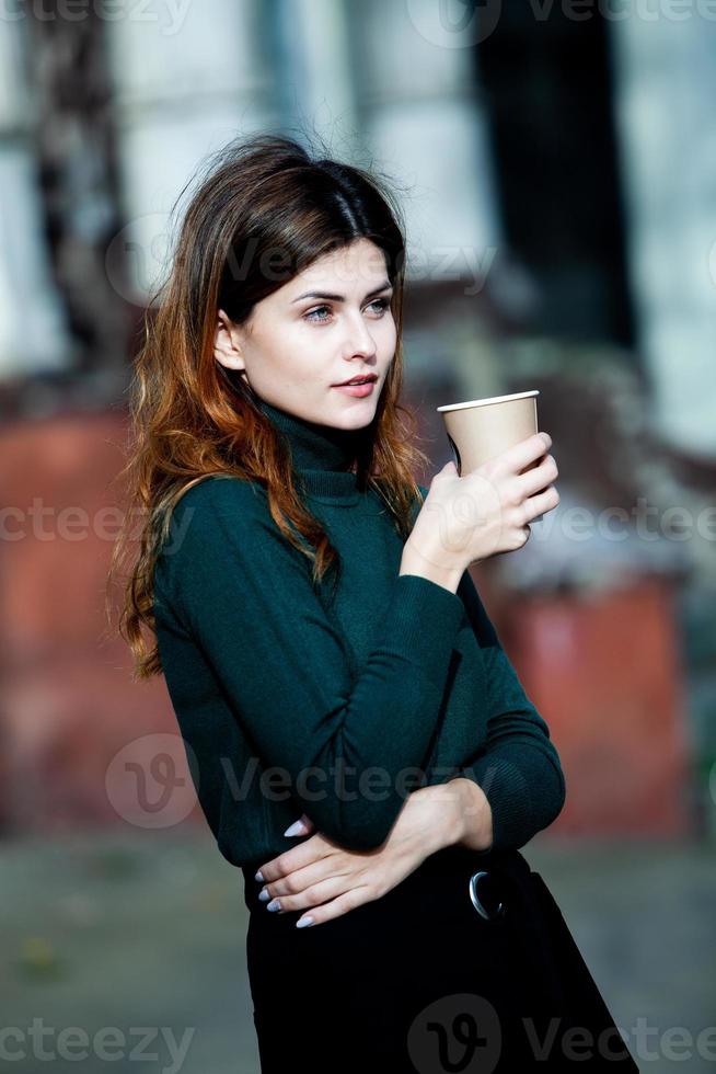 giovane donna alla moda che beve il tè in una strada della città. ragazza europea hipster con bicchiere di carta latte. splendida giovane donna con una tazza di caffè in una strada di città. pausa caffè. caffè da portar via. foto