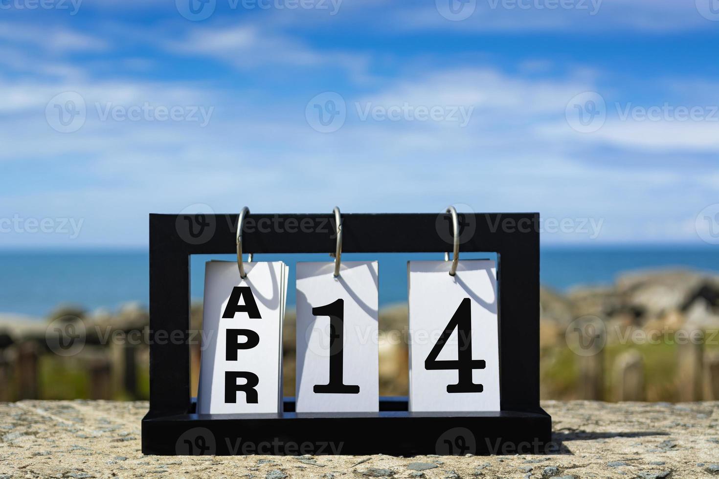 14 aprile testo della data del calendario su telaio in legno con sfondo sfocato dell'oceano. foto
