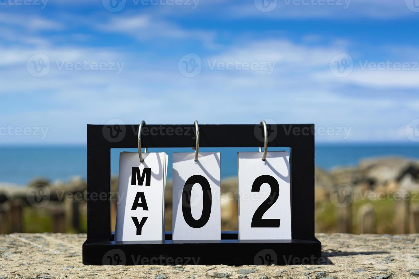 02 maggio testo della data del calendario su cornice di legno con sfondo sfocato dell'oceano. foto