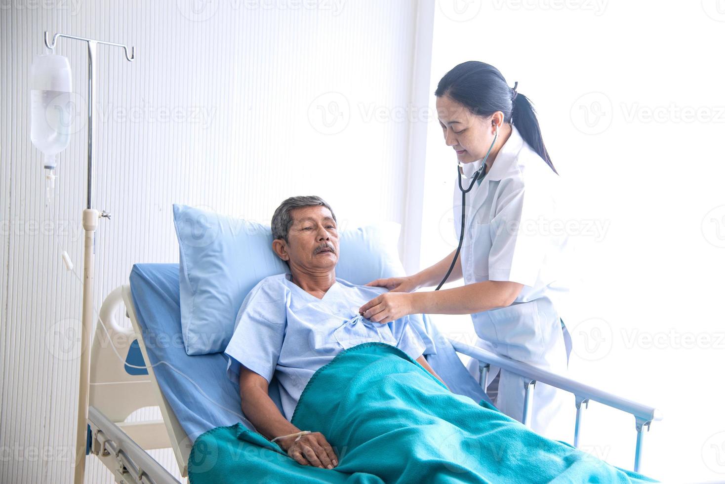 medico professionista donna asiatica con blocco note che sorride, visita, parla e diagnostica il paziente anziano sdraiato nel letto del paziente in reparto ospedaliero foto