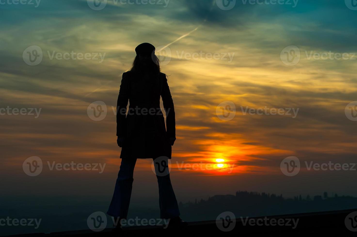 ragazza in piedi sul muro che guada il tramonto rosso foto