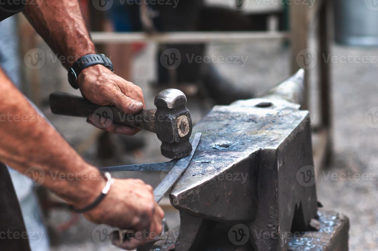 un fabbro artigiano bussa con un martello sul ferro per dare forma foto