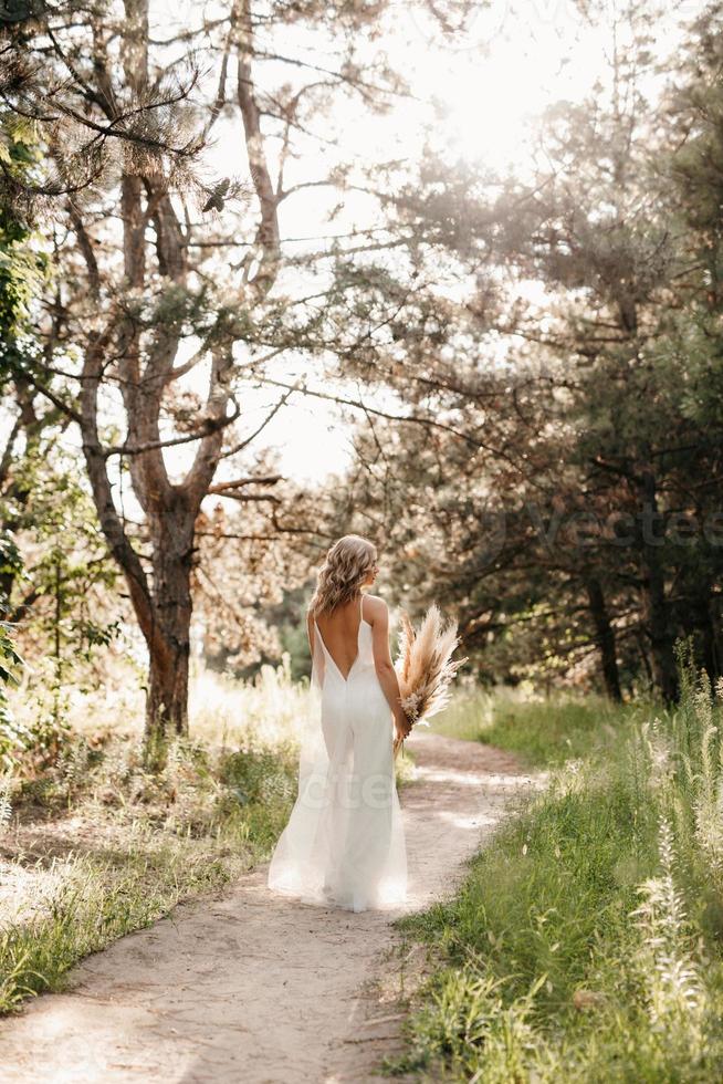 ragazza felice della sposa in un vestito bianco chiaro con un mazzo di fiori secchi foto