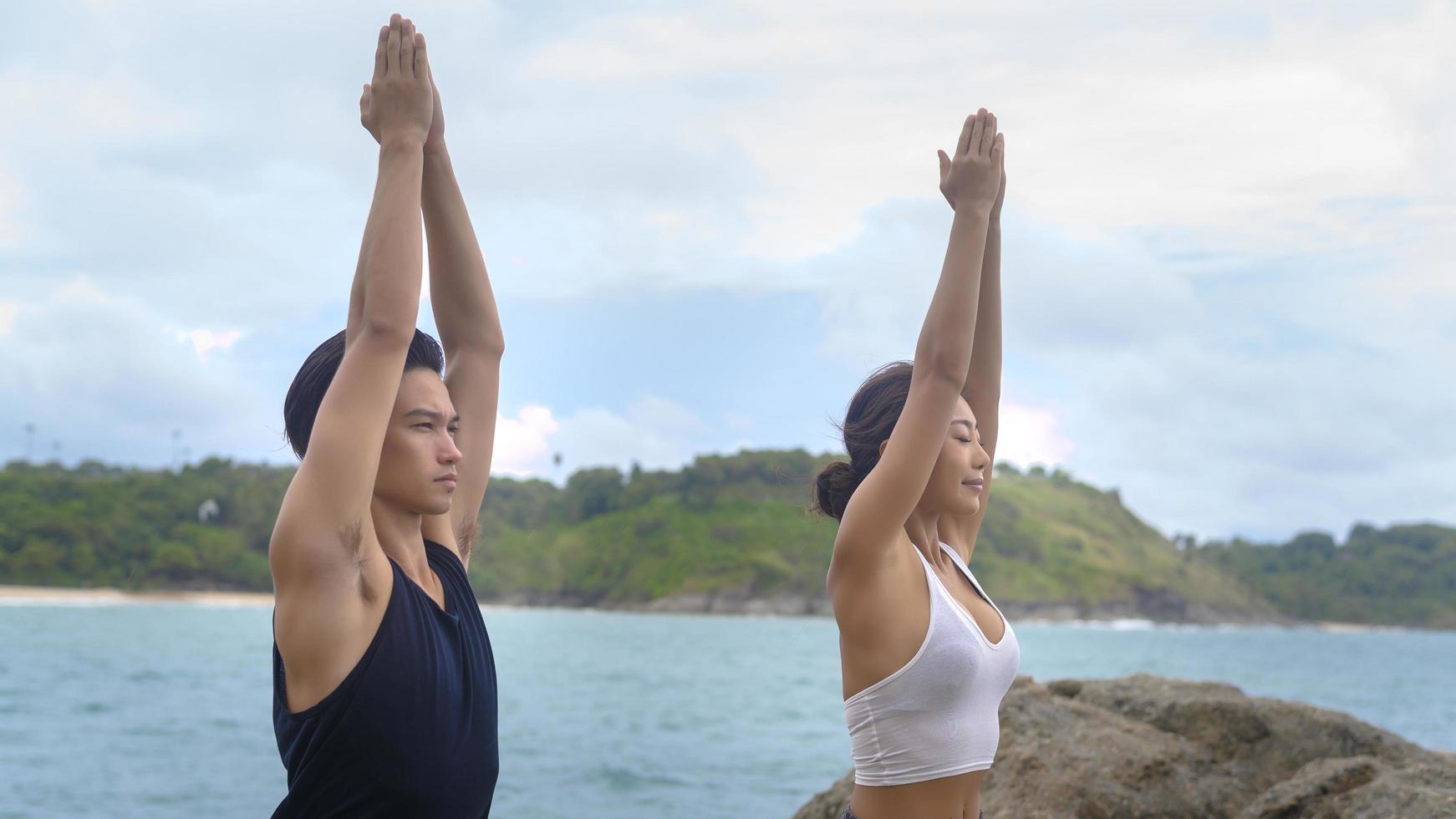 giovane uomo e donna in abiti sportivi che fanno yoga sulla roccia al mare, concetto di salute e meditazione foto