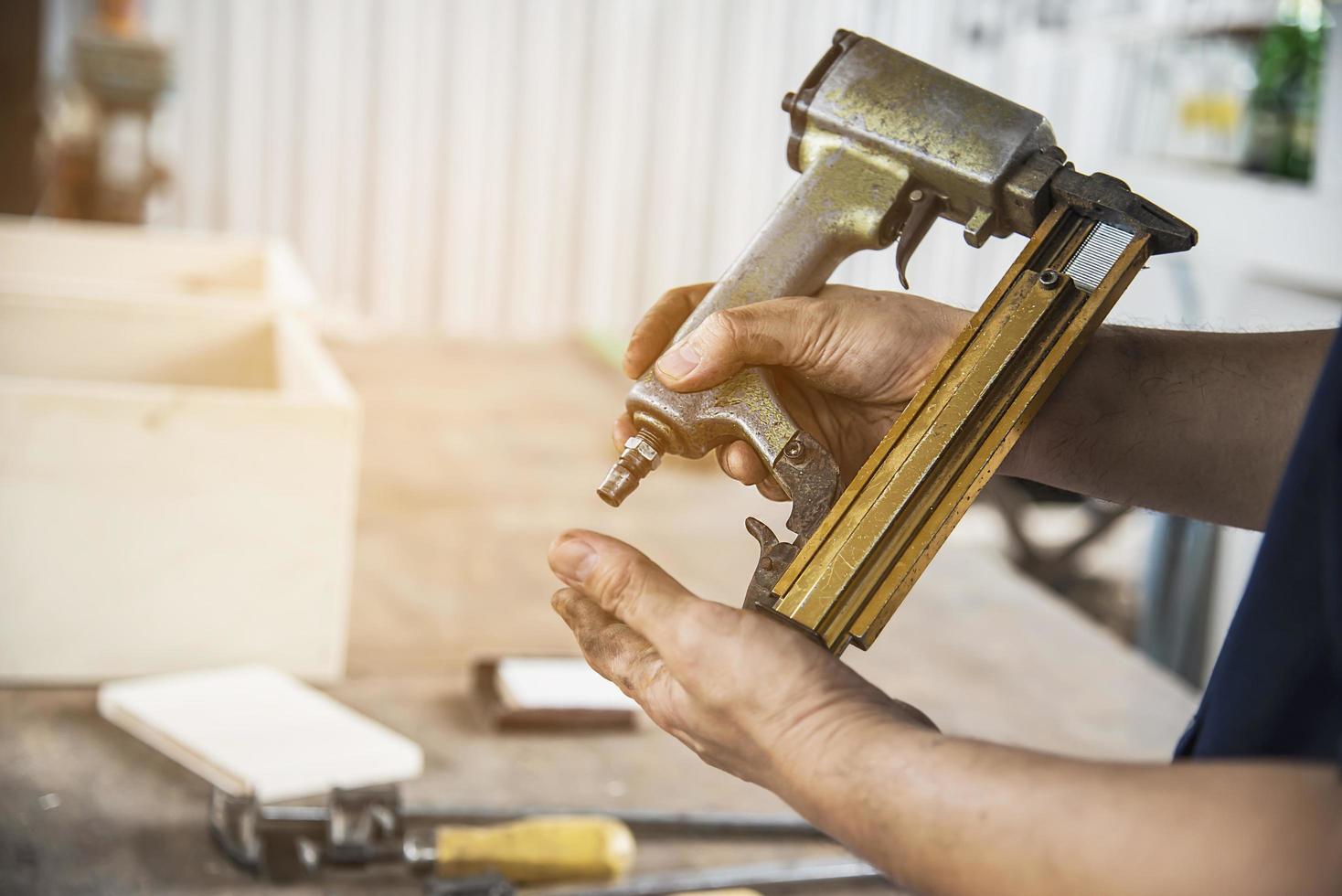 falegname che usa una pistola sparachiodi ad aria che fa lavori di mobili in legno foto