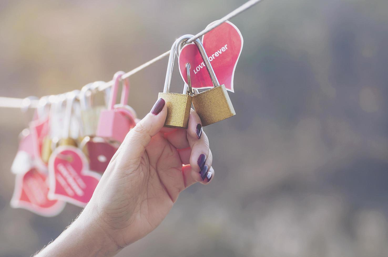 chiave del lucchetto della tenuta della mano della signora con il simbolo del cuore dell'amore sul ponte - concetto di simbolo del segno della cultura di amore foto