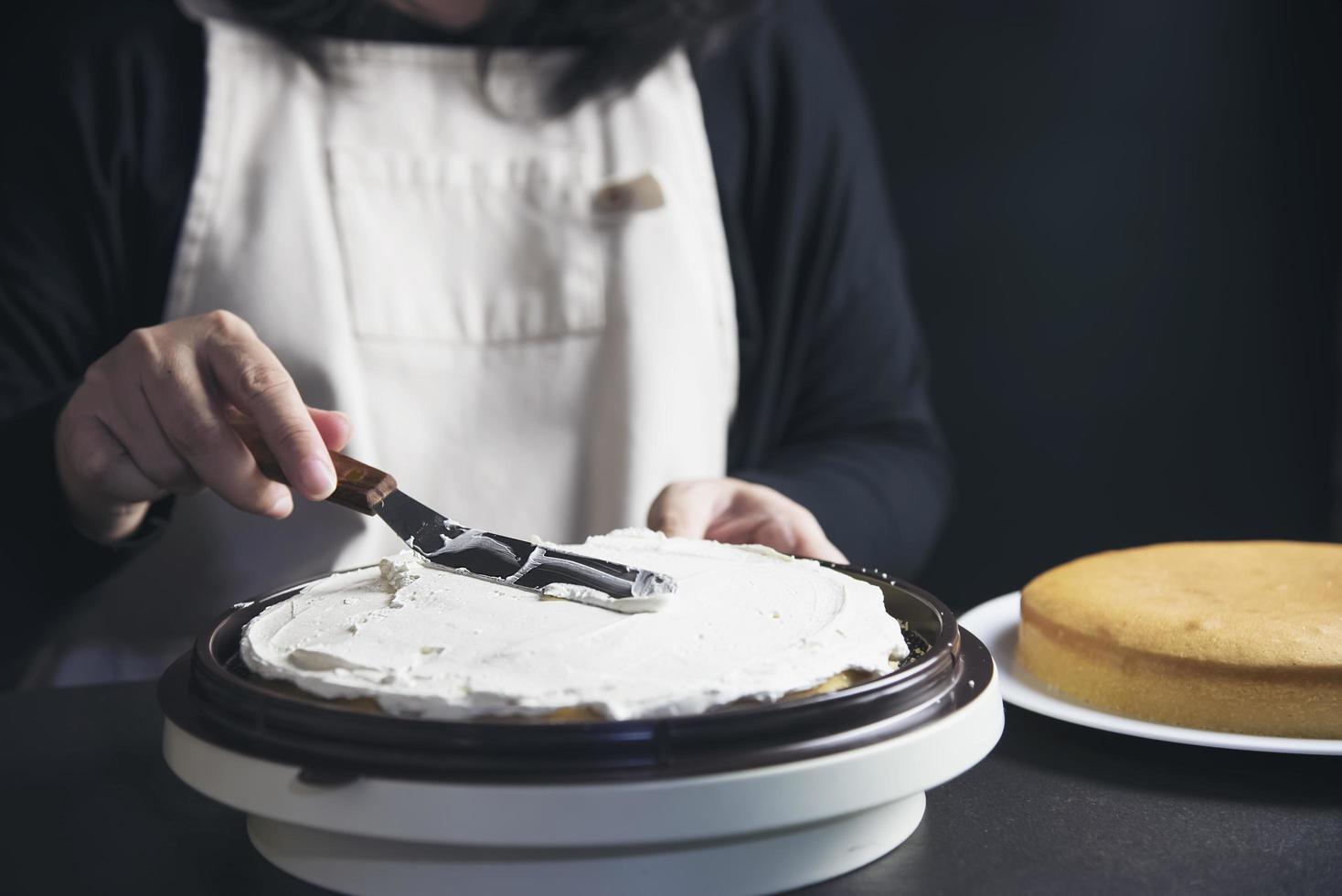 signora che fa la torta mettendo la crema con la spatola - concetto di cucina da forno fatto in casa foto