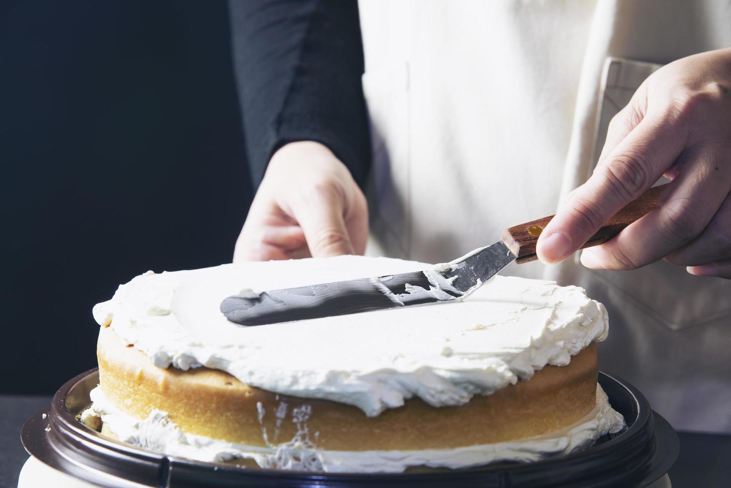 signora che fa la torta mettendo la crema con la spatola - concetto di cucina da forno fatto in casa foto