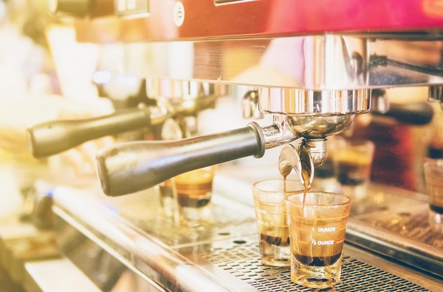 foto d'epoca di una macchina per caffè in primo piano parzialmente con quattro colpi di caffè fresco con luce calda dall'angolo in alto a sinistra