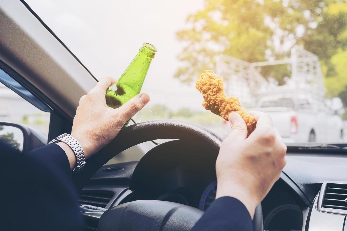 uomo che beve birra e mangia pollo fritto mentre guida un'auto foto