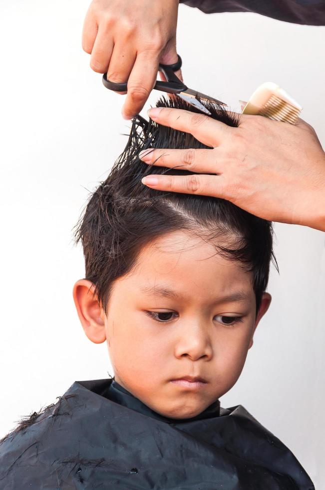 un ragazzo viene tagliato i capelli da un parrucchiere su sfondo bianco, concentrarsi sugli occhi a destra foto