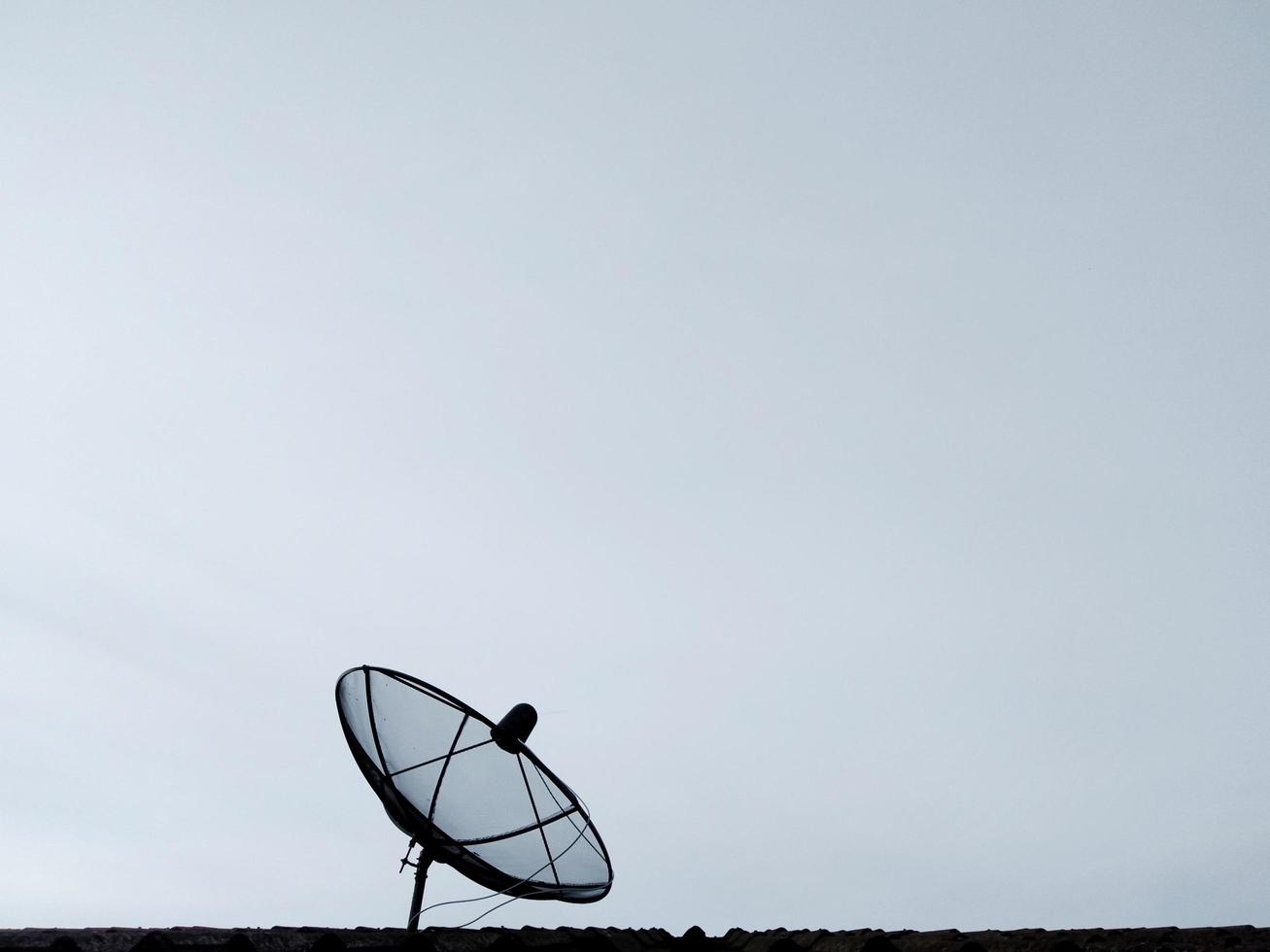 parabola satellitare nera sul tetto della casa cielo nuvoloso in una giornata con tempo inclemente foto