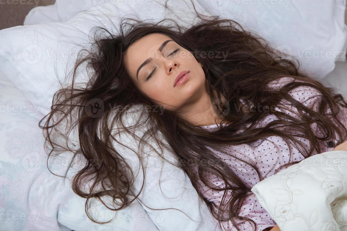 la ragazza dorme in un letto bianco a casa. giovane donna che dorme in indumenti da notte sulla biancheria bianca a letto a casa, vista dall'alto. foto