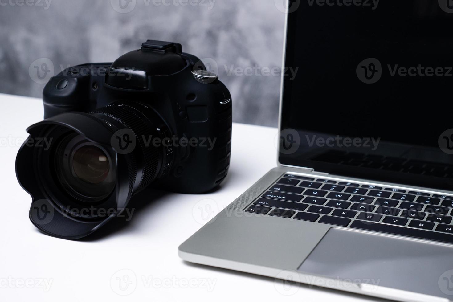 una fotocamera digitale nera e un computer portatile su un tavolo. foto