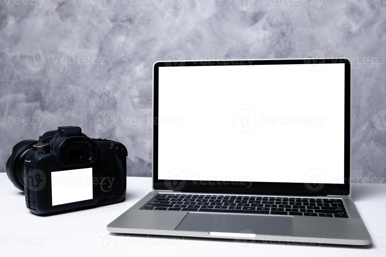 una fotocamera digitale nera e un computer portatile su un tavolo foto