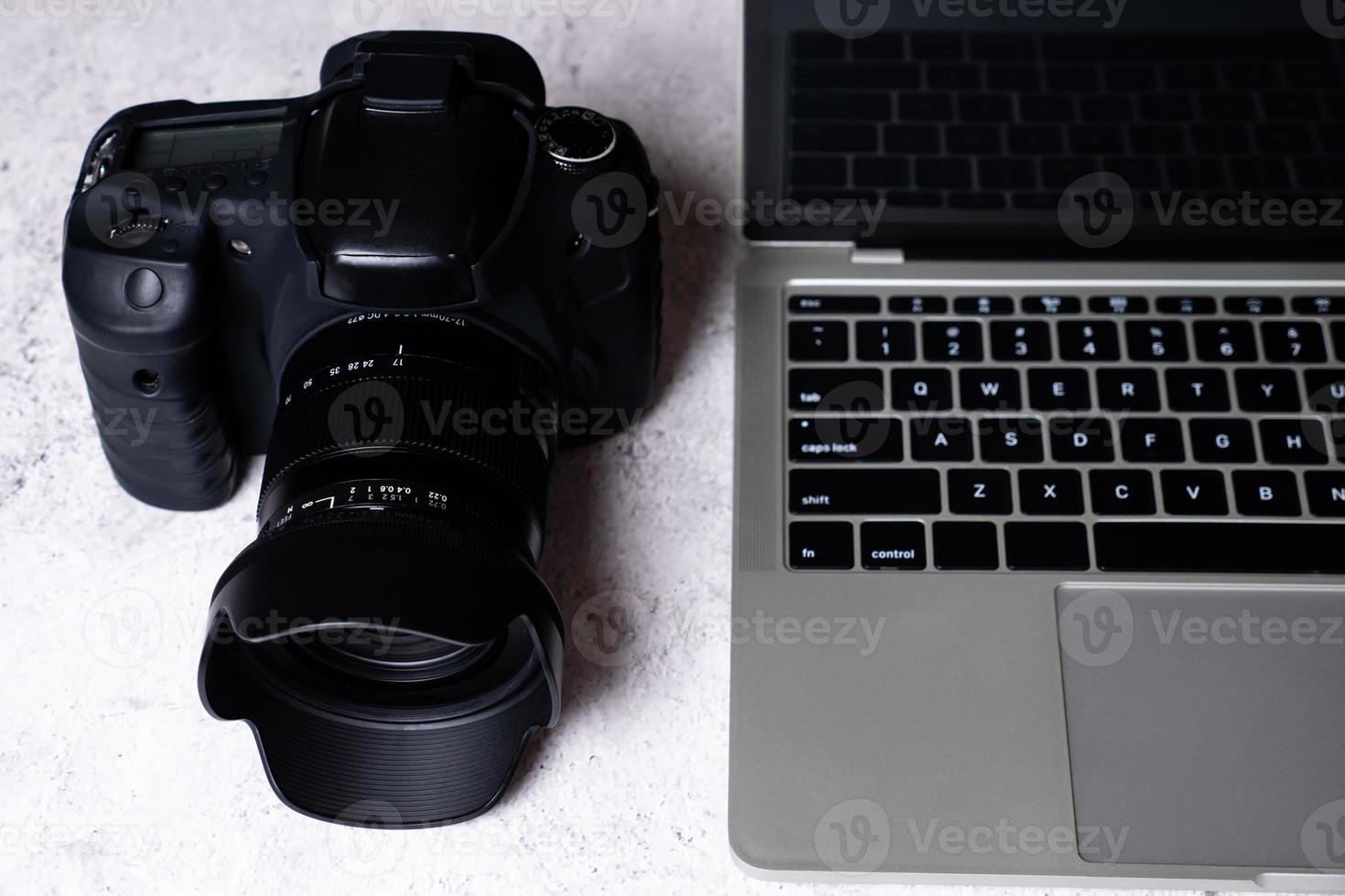 una fotocamera digitale nera e un computer portatile su un tavolo. foto