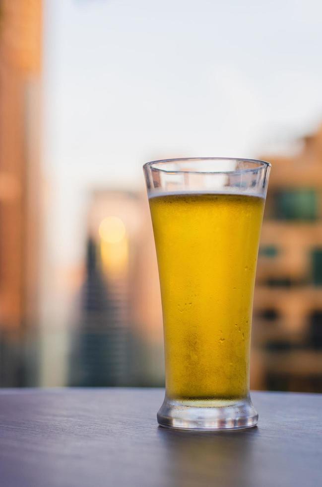 un bicchiere di birra viene messo sul tavolo al bar sul tetto con sfondo sfocato della città. foto