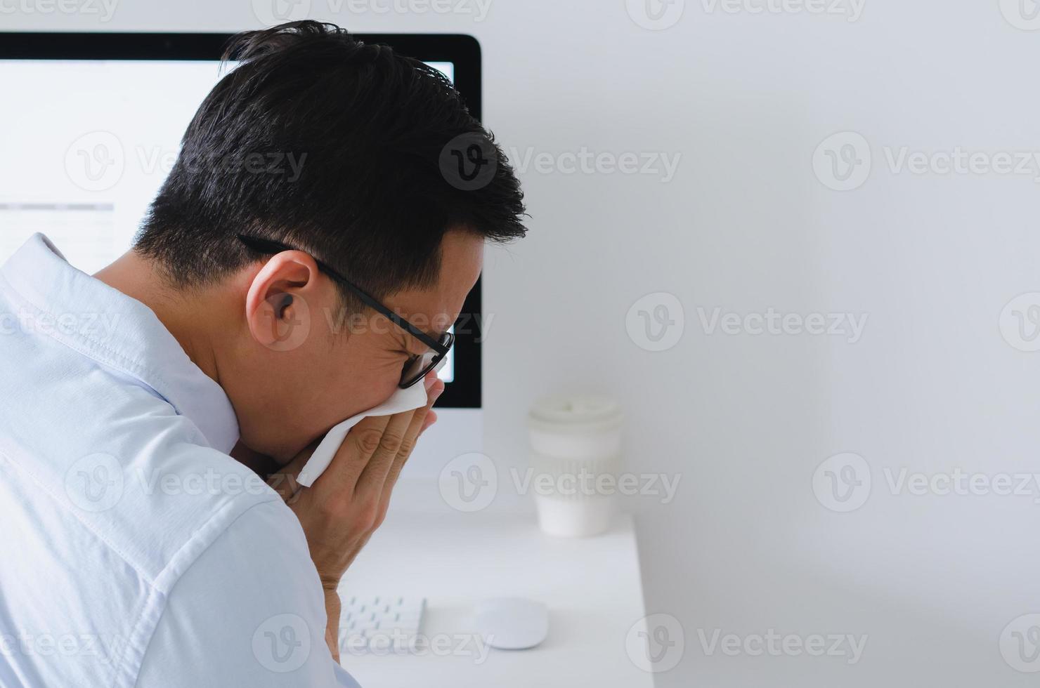 uomo asiatico che starnutisce sul tovagliolo sul posto di lavoro per il concetto di influenza e virus. foto