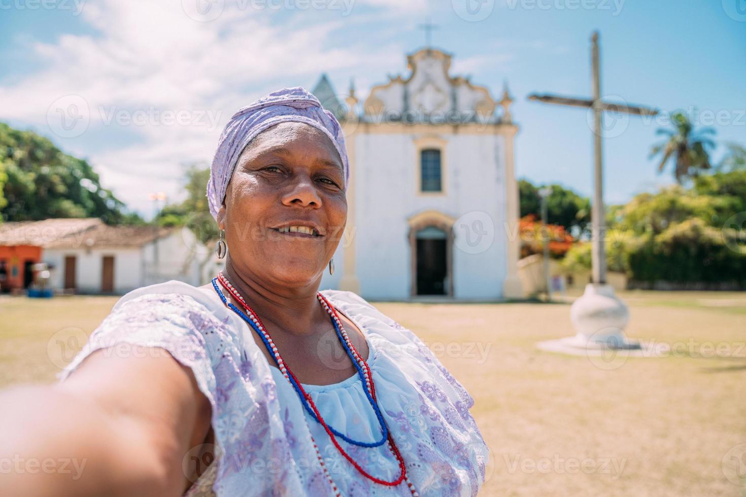 felice donna brasiliana di origine africana vestita con il tradizionale abito bahiano che fa un selfie davanti alla chiesa. concentrarsi sul viso foto